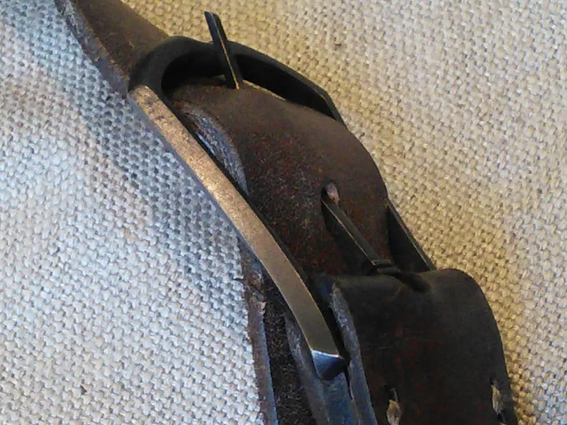 A long cast buckle on a dark leather strap, against linen